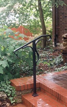 an iron handrail on the steps leading to a brick building with trees in the background