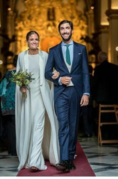 a man and woman are walking down the aisle at an event with flowers in their hand