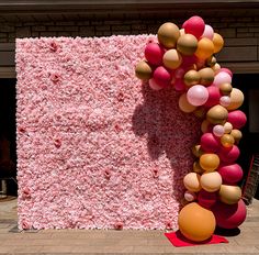 a pink wall with balloons hanging from it's sides and a red rug on the ground