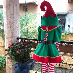 a woman dressed in green and red standing next to a potted plant on a balcony