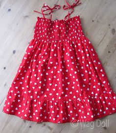 a red dress with white hearts on it sitting on the floor next to a wooden floor