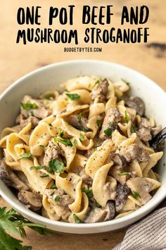 a white bowl filled with pasta and mushrooms on top of a wooden table next to parsley