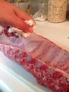 a person is holding a piece of raw meat in plastic wrap on a counter top