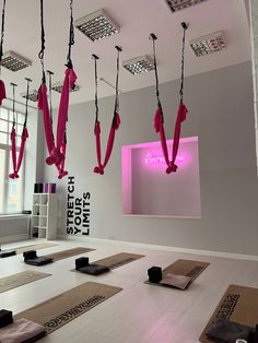 yoga mats are lined up in the middle of a room with pink lights hanging from the ceiling