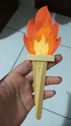 a hand holding a matchstick with a paper fire on it's tip and flames coming out of the top