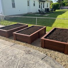 four wooden boxes filled with dirt in front of a fenced yard and white house