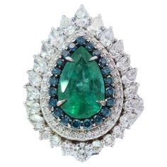 Elevate your jewelry collection with this extraordinary pear-shaped emerald ring, a true embodiment of luxury and refined artistry. At its heart lies a vibrant 2.61-carat emerald, whose deep green hue exudes a natural allure that is both captivating and timeless. This stunning centerpiece is elegantly framed by an intricate arrangement of blue and white diamonds, totaling 2.60 carats. The combination of these contrasting colors creates a mesmerizing play of light, enhancing the ring’s overall br Luxury Pear-shaped Emerald Wedding Ring, Art Deco Pendant Necklace, Pear Shaped Diamond Ring, Diamond Pendent, Pear Shaped Ring, Modern Engagement Rings, Art Deco Necklace, Fancy Diamonds, Brown Diamond