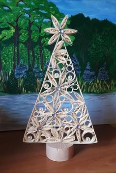 a christmas tree made out of paper sitting on top of a wooden table next to a painting