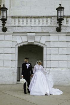 a bride and groom are standing in front of a white stone building with black lanterns