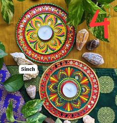 two colorful plates sitting on top of a table next to some plants and rocks with candles in them