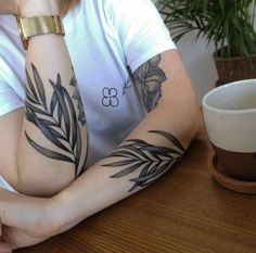 a woman sitting at a table with her arms crossed and tattoos on her arm, next to a coffee cup