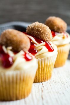 three cupcakes with white frosting and red sauce on top are sitting on a table