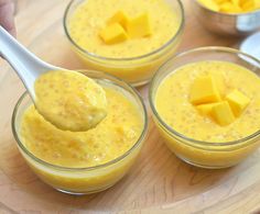 three small glass bowls filled with yellow pudding and topped with chunks of cheese on a wooden table