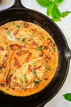 a skillet filled with chicken covered in sauce and garnished with green leaves