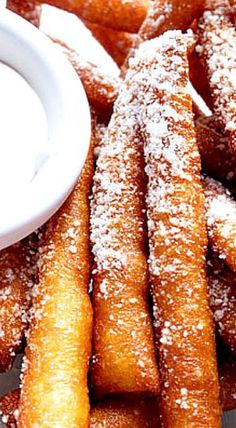 powdered sugar coated churros on a plate with dipping sauce