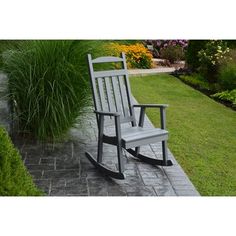 a wooden rocking chair sitting on top of a stone walkway next to a lush green field