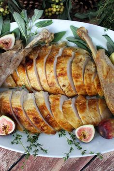 a white plate topped with sliced up meat and figs next to green leaves on top of a wooden table