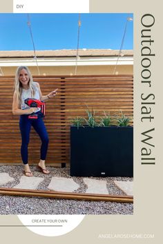 a woman standing in front of a wooden fence holding a red and black object with one hand