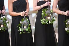 two women in black dresses holding lanterns with greenery on them and one wearing a ring