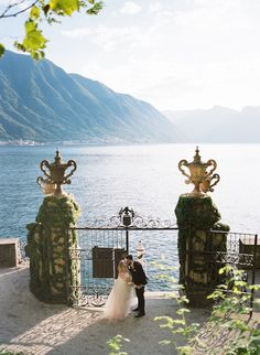 a bride and groom standing next to each other in front of an iron gate overlooking the water