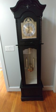 a grandfather clock sitting on top of a wooden floor next to a wall with a mirror