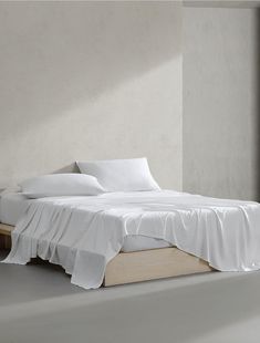 a bed with white sheets and pillows in a room next to an open window on the floor