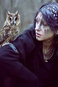 a woman with face paint and an owl sitting on her arm in front of her