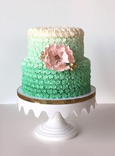 there is a green and white cake with flowers on the top, sitting on a pedestal