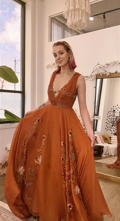 a woman standing in front of a window wearing an orange dress with flowers on it