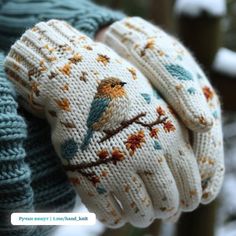 a pair of white knitted gloves with birds on them, sitting on a tree branch