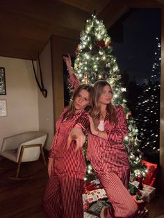 two women in matching pajamas standing next to a christmas tree