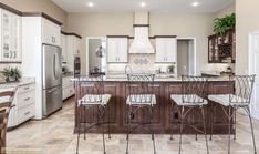 a large kitchen with white cabinets and marble counter tops, an island in the middle is flanked by four bar stools