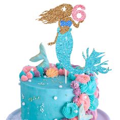 a birthday cake decorated with blue frosting and pink icing, featuring a mermaid holding a donut