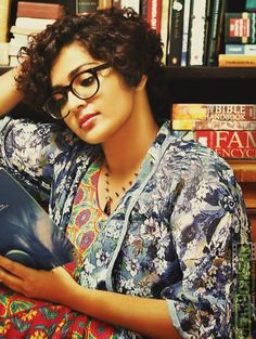 a woman sitting in front of a bookshelf holding a book