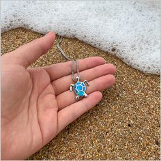 a person is holding a turtle necklace in their hand on the sand at the beach