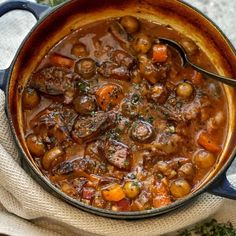 a pot filled with stew sitting on top of a white cloth next to a wooden spoon