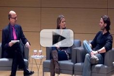 two men and a woman sitting on couches in front of a wall talking to each other