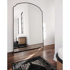 a large mirror sitting on top of a wooden floor next to a rug and window