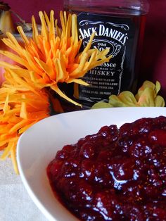 a white bowl filled with cranberry sauce next to flowers and a bottle of jack daniels