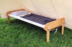 a wooden bed sitting on top of a lush green field next to a white tent