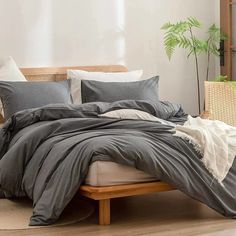 an unmade bed with grey linens and white pillows on the bottom, next to a potted plant