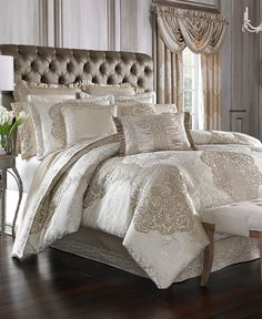 a bed with white and gold comforters in a bedroom next to a chair, chandelier and window