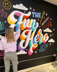 a woman standing in front of a wall with the words'the fun here'painted on it