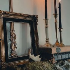 two candles are lit next to an old book on a mantle with moss and fake antlers