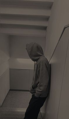 a person in a hoodie leaning against a wall with their back to the camera