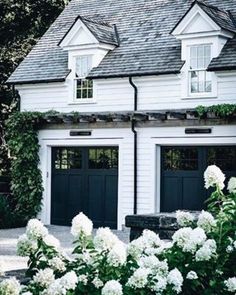 a white house with two black garage doors and some flowers in front of the building