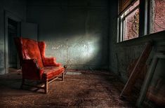 an old red chair sitting next to a window in a room with peeling paint on the walls