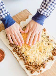 a person is kneading shredded cheese on top of a pizza dough with their hands