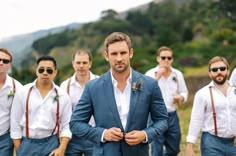 a group of men standing next to each other in front of trees and mountains with sunglasses on