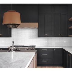 a kitchen with black cabinets and white marble counter tops is pictured in this image, there are two pendant lights hanging over the sink